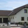 Fam. Zelenka, © Zelenka Ein modernes Einfamilienhaus mit braunem Dach und hellem Anstrich, umgeben von Bäumen und einem Zaun.