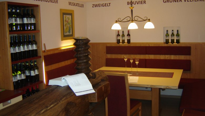 Weingut Fahrnecker, © Weingut Fahrnecker Innenansicht eines Weinguts mit Tisch, Stühlen und Weinregalen.