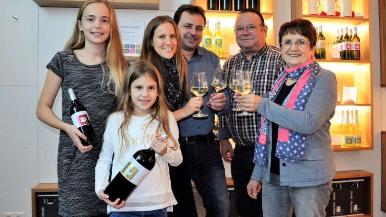 Weinbau Holzer, © Weinbau Holzer Familie mit Weinflaschen und Gläsern in einem Weinkeller.