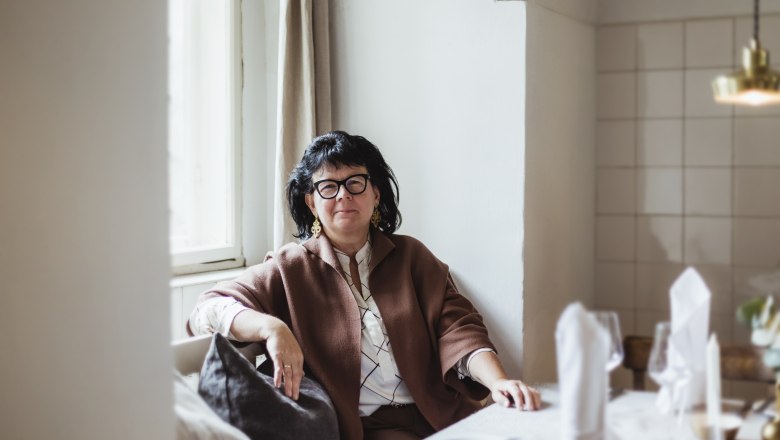 Wirtin Sandra Blauensteiner, © Niederösterreich Werbung/David Schreiber Frau sitzt an einem gedeckten Tisch in einem gemütlichen Raum.