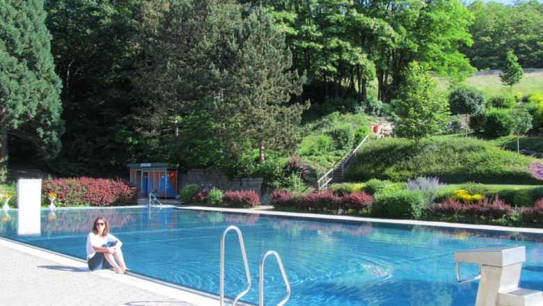 Waldbad Wölbling, © Marktgemeinde Wölbling Frau sitzt am Rand eines Freibads mit Wald im Hintergrund.