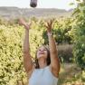 TDR-Weingut Haimel, © Cornelia Wurst Frau wirft Weinflasche in die Luft in einem Weinberg.