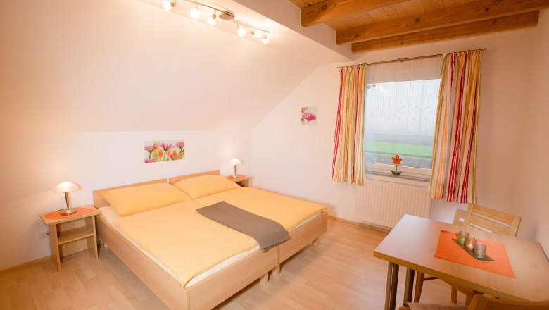 Ferienwohnung Muck, © schwarz-könig.at Gemütliches Schlafzimmer mit Doppelbett, Holzbalkendecke und Tisch mit Stühlen.