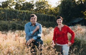 hofmann-2022, © David Schreiber Zwei Personen in einem Weinberg, eine hält eine Weinflasche, die andere ein Weinglas.