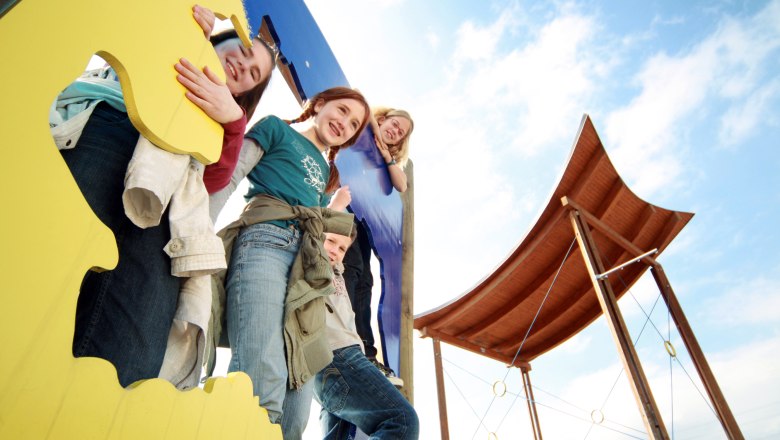 Kapelln, © weinfranz.at Kinder spielen auf einem bunten Klettergerüst mit einem Holzdach im Hintergrund.
