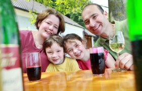 Roman Winter, © Weinfranz.at Familie sitzt an einem Tisch im Freien und lächelt in die Kamera.