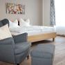 Schlafzimmer, Bett & Rad Schöpf, Traismauer, © Familie Schöpf Grauer, gemütlicher Stuhl im Vordergrund. Im Hintergrund ein Doppelbett mit weißer Bettwäsche.