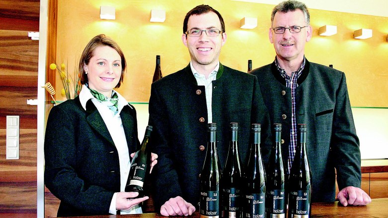 Weingut Holzer, © z.V.g. Fam. Holzer Drei Personen stehen hinter einem Tisch mit Weinflaschen im Weingut Holzer.