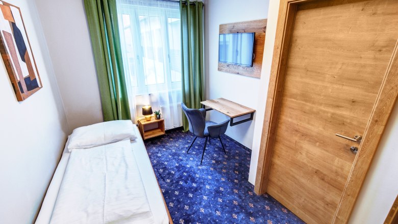 Einzelzimmer mit Schreibtisch und Fenster, blauer Teppich