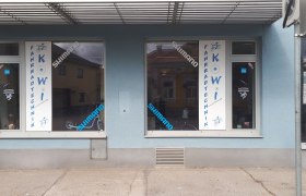 Fahrradgeschäft mit blauer Fassade und Schaufenstern mit Aufschrift 'Fahrradtechnik KOWI'.