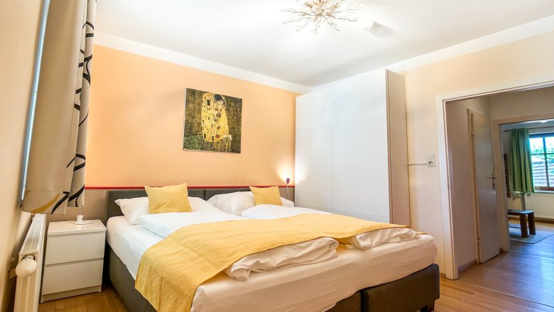 Schlafzimmer mit Doppelbett, gelber Bettwäsche und Kunstwerk an der Wand.