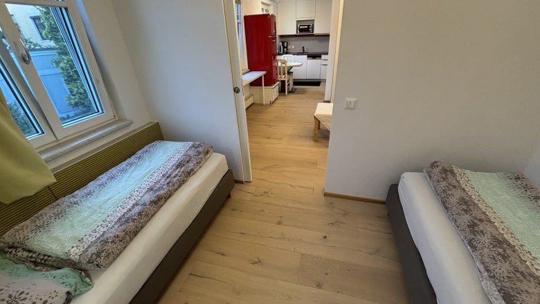 Schlafzimmer mit zwei Einzelbetten und Blick in die Küche.