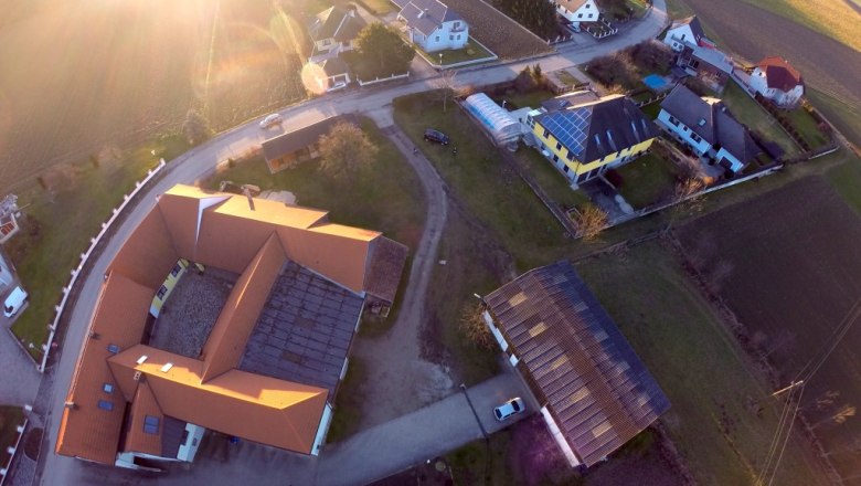 Luftaufnahme eines Dorfes mit Häusern, Straßen und Feldern bei Sonnenuntergang.