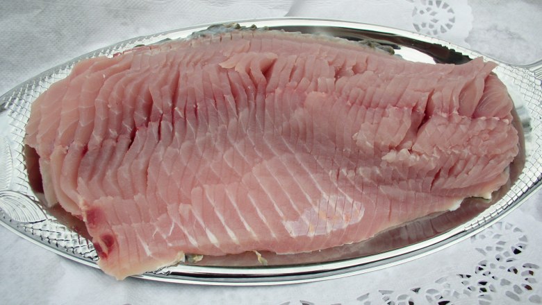 Ein rohes Karpfenfilet auf einem silbernen Tablett, umgeben von Spitzenpapier.