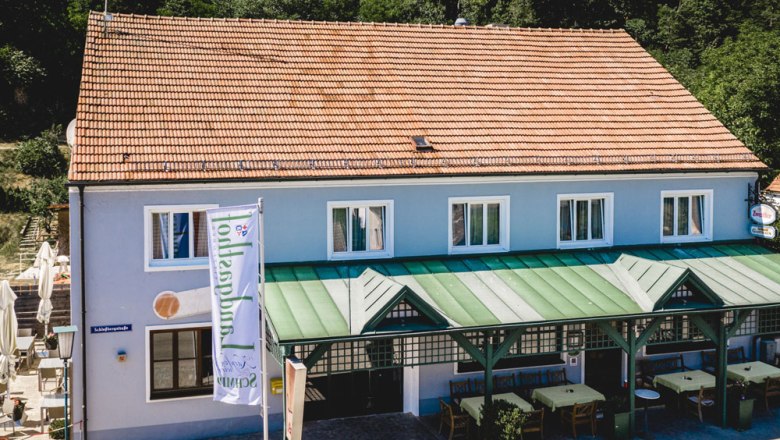 Blaues Gebäude mit rotem Dach und grünem Vordach, Restaurantbereich außen.