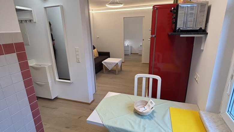 Kleines Wohnzimmer mit Esstisch, St&uuml;hlen, rotem K&uuml;hlschrank und Sofa.