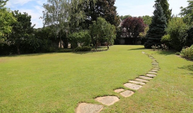 Ein gepflegter Garten mit einem geschwungenen Steinweg und Bäumen im Hintergrund.