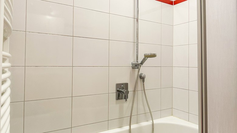 Badezimmer mit Badewanne, Duschkopf und roten Fliesen.