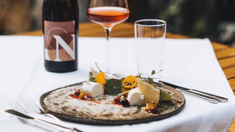 Ein Teller mit Käse und Garnitur, ein Glas Roséwein und eine Weinflasche auf einem Tisch.