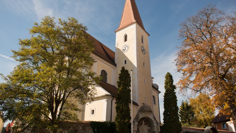 Kirche mit Turm und Uhr, umgeben von Bäumen im Herbst.