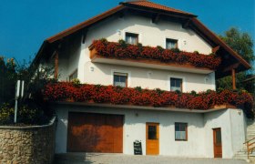 Ein zweistöckiges Gästehaus mit roten Blumen auf den Balkonen.