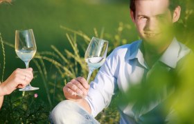 Zwei Personen stoßen mit Weingläsern im Freien an.