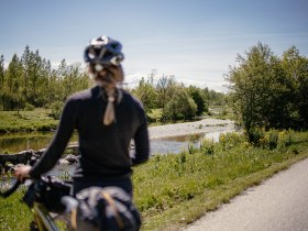 Ein sanfter Radweg schl&auml;ngelt sich entlang des glitzernden Wassers, umgeben von &uuml;ppigem Gr&uuml;n und bl&uuml;henden Wiesen. Die frische Luft und die sanften Ger&auml;usche der Natur laden dazu ein, die Seele baumeln zu lassen und die Sch&ouml;nheit der Landschaft zu genie&szlig;en.