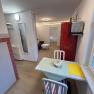 Kleines Wohnzimmer mit Esstisch, Stühlen, rotem Kühlschrank und Sofa.
