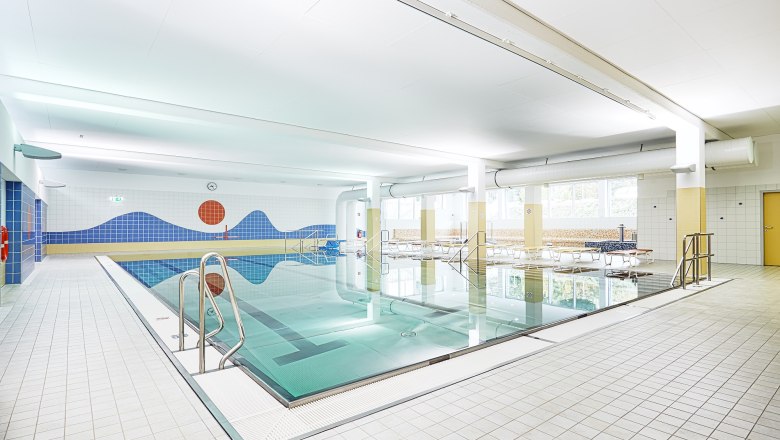 Innenansicht eines Hallenbads mit Schwimmbecken und blauer Wanddekoration.