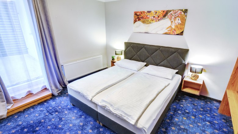 Doppelzimmer mit blauem Teppichboden und großem Fenster