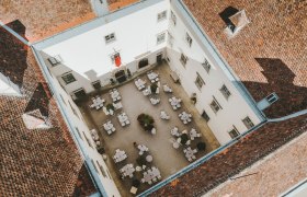 Luftaufnahme eines Innenhofs mit Tischen und Stühlen, umgeben von einem Gebäude mit roten Ziegeldächern.