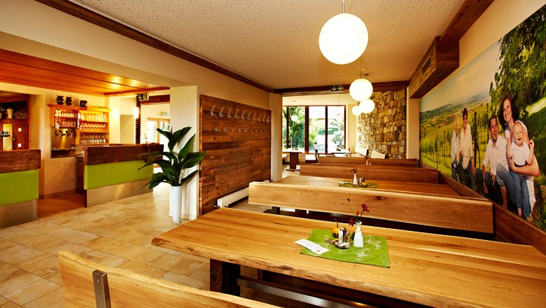 Innenansicht eines gemütlichen Restaurants mit Holztischen und -bänken, dekoriert mit Pflanzen und einem großen Wandbild.