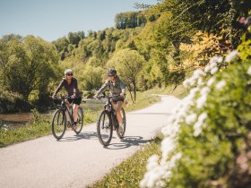 Zwei Radfahrerinnen fahren entlang des Traisental-Radwegs, der durch bewaldetes Gebiet f&uuml;hrt.