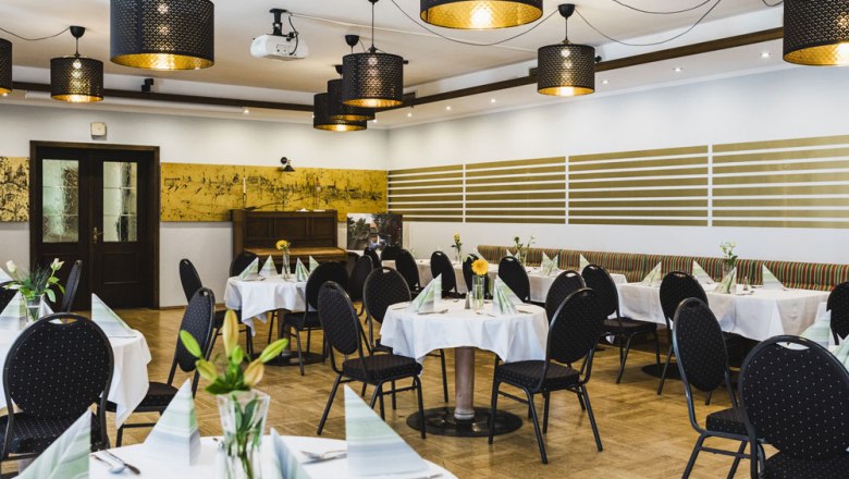 Elegantes Restaurant mit runden Tischen, weißen Tischdecken und modernen Lampen.