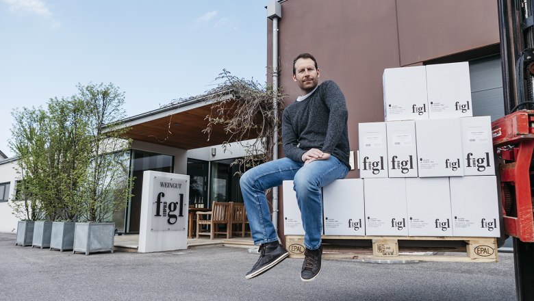 Ein Mann sitzt auf gestapelten Weinkartons vor dem Weingut Leopold Figl.