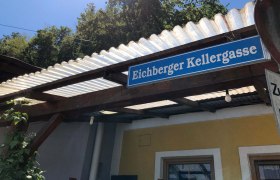Schild mit der Aufschrift 'Eichberger Kellergasse' an einem Gebäude mit Wellblechdach.