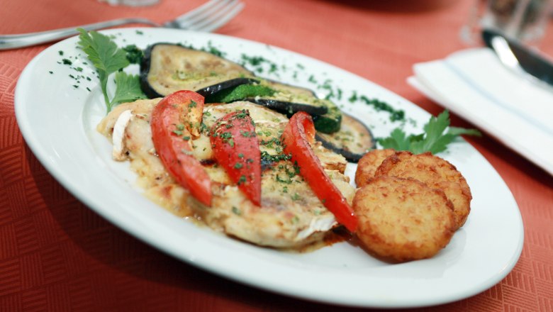 Ein Teller mit gebratenem Gem&uuml;se, Tomaten und R&ouml;sti auf einem roten Tisch.