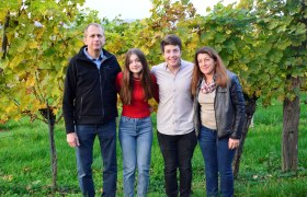 Vier Personen stehen lächelnd vor Weinreben im Freien.