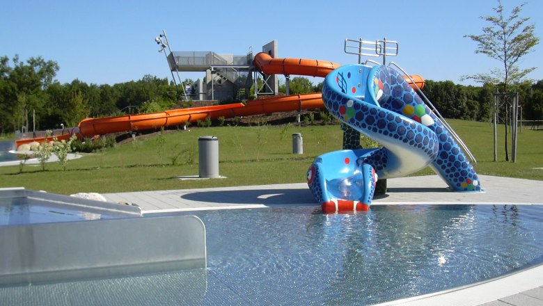 Blick auf einen Aquapark mit blauer Kinderrutsche und großer oranger Wasserrutsche im Hintergrund.