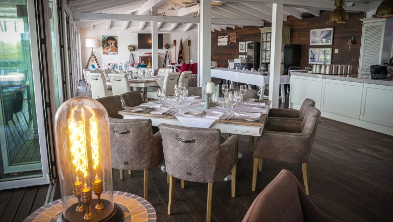 Gedeckter Tisch im Speisesaal. IM Vordergrund eine Leuchte. Der Saal ist in Weiß und braun gehalten.