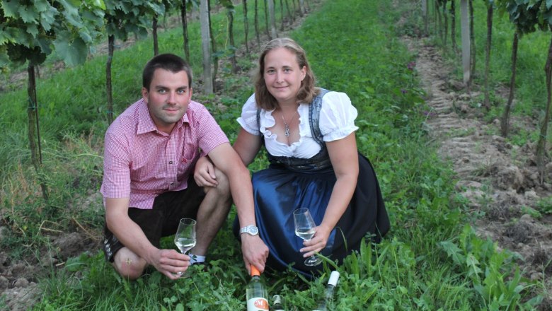 Zwei Personen sitzen in einem Weinberg mit Weingl&auml;sern und Flaschen.