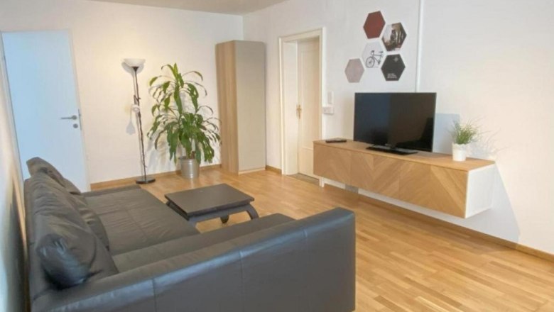 Wohnzimmer mit schwarzer Couch und Flach TV