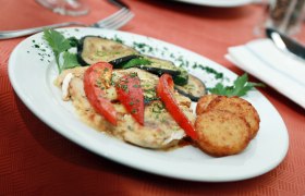 Ein Teller mit gebratenem Gemüse, Tomaten und Rösti auf einem roten Tisch.