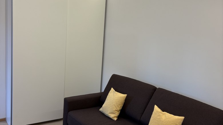 Modernes Wohnzimmer mit braunem Sofa, gelben Kissen und kleinem Tisch mit wei&szlig;er Tischdecke.