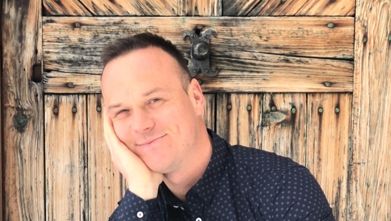 Person lehnt sich l&auml;chelnd an eine alte Holzt&uuml;r.