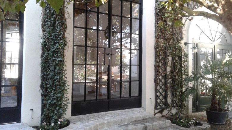 Eingangsbereich mit großen Glasfenstern, Efeu und Pflastersteinen.