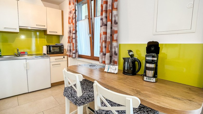 Moderne Küche mit grüner Rückwand, weißen Schränken, Holztheke und Kaffeemaschine.