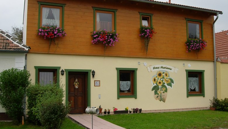 Zweist&ouml;ckiges Haus mit Holzverkleidung und Blumenk&auml;sten, beschriftet als 'Haus Marianne'.