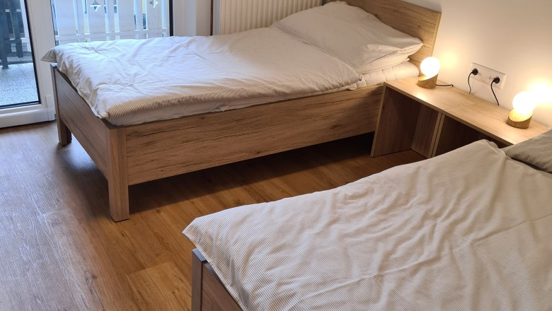 Zwei Einzelbetten in einem hellen Zimmer mit Holzboden und Balkonzugang.