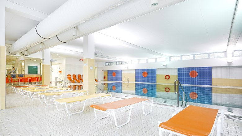 Innenansicht eines Hallenbads mit Liegestühlen und Schwimmbecken.